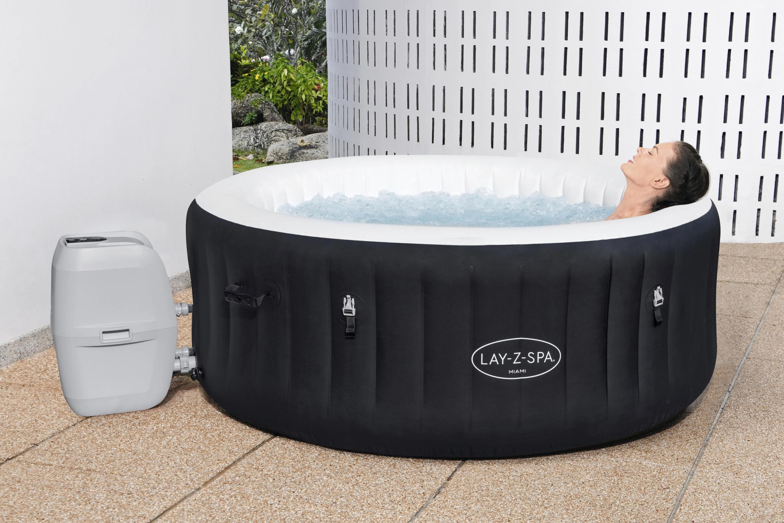 Inflatable hot tub with a person inside, featuring the Lay-Z-Spa brand, on a tiled patio.