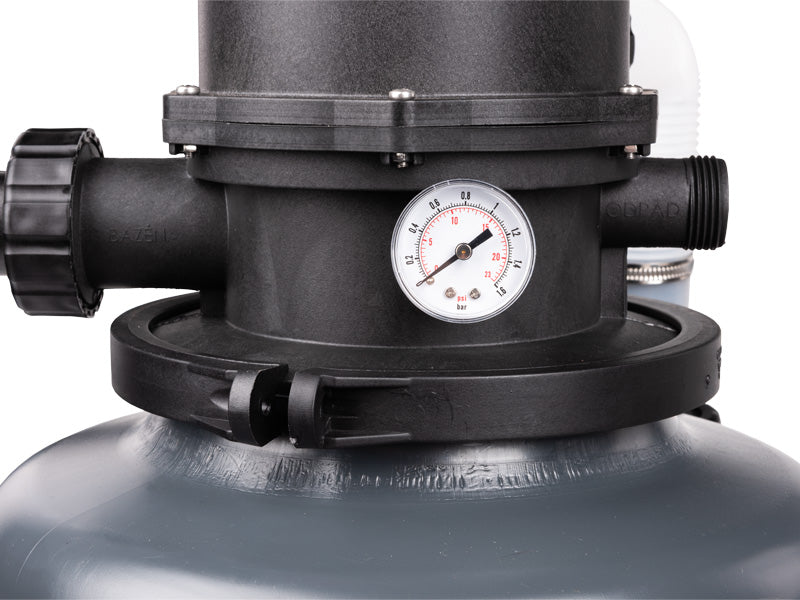 Close-up of a black sand filter pressure gauge and valve assembly connected to a gray sand tank, on a white background.