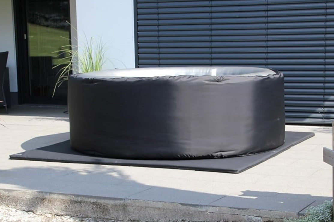 Black hot tub on a patio area with plants and a building in the background