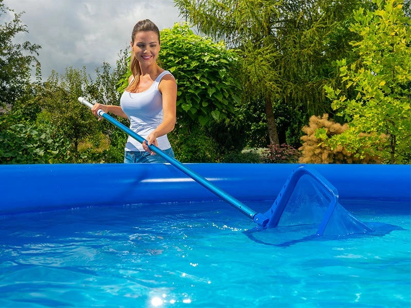 Woman cleaning an above-ground pool with a net in a garden setting