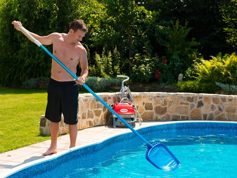 Man cleaning a pool with a skimmer net in a garden setting