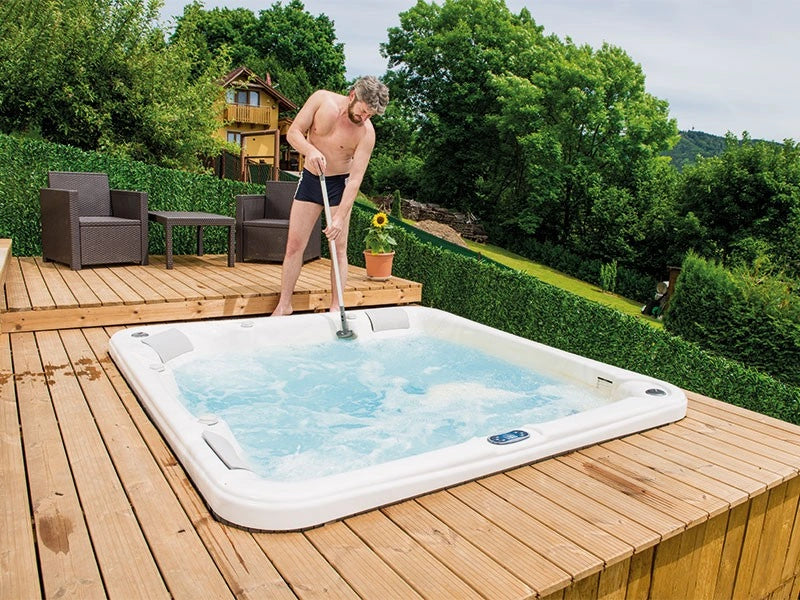 Man cleaning a hot tub on a wooden deck with greenery in the background