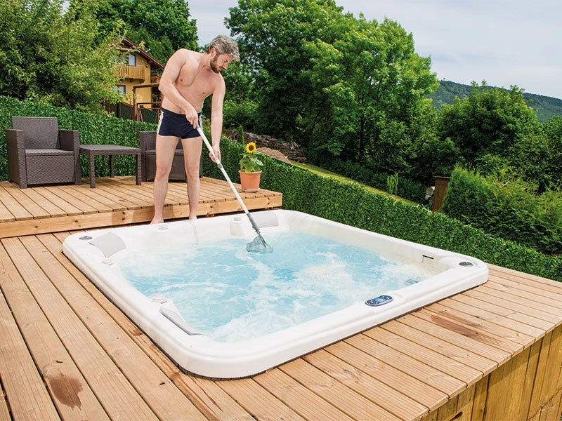 Man cleaning an hot tub on a wooden deck with greenery in the background