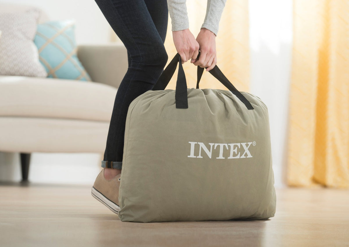 Person holding an Intex branded air mattress in a living room setting