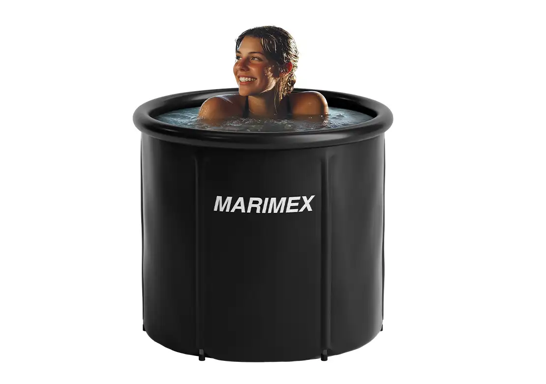 A woman smiling while sitting in a black round outdoor hot tub with water, featuring the MARIMEX logo on the front, set against a solid white background.